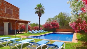 A swimming pool with blue lounge chairs, a stone building, and flowering trees.