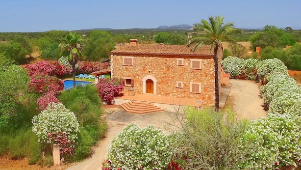 A stone house with a pool, surrounded by lush greenery and flowering plants.