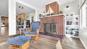 A living room with a fireplace, a bookshelf, and a dining area.