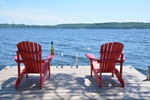Une jetée en bois avec deux chaises Adirondack rouges et une bouteille de vin sur une table.