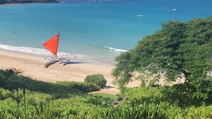 Uma praia com águas turquesa cristalinas, uma orla arenosa e vegetação exuberante em primeiro plano.