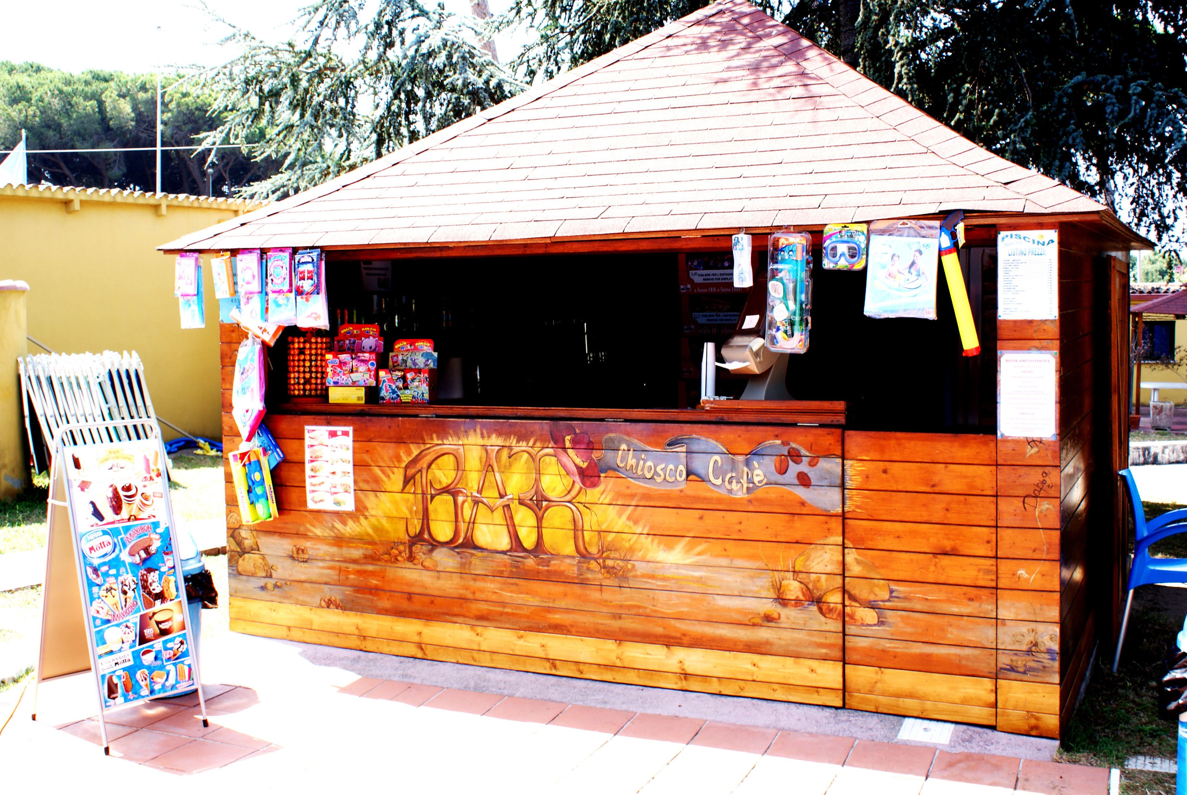 A small wooden kiosk with a sloped roof, featuring a mural of a dog and the words "Chiosco Cafe."