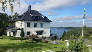 Una casa de dos pisos con balcón, césped y vista al lago.