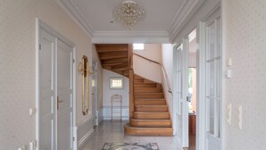 Un pasillo con escalera de madera, puertas blancas y un candelabro.