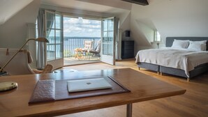 Un dormitorio con cama, escritorio con una laptop, silla y balcón con mobiliario exterior.
