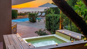 Un jacuzzi con velas, una terraza de madera y vistas al atardecer sobre el océano.