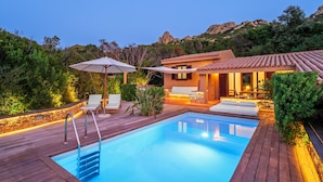 Una piscina con un deck de madera, sillas de descanso y un área de patio con una mesa y sillas.