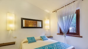 Habitación de hotel con cama, dos lámparas de noche, una ventana con cortinas y un espejo en la pared.