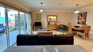 Sala de estar com sofá, mesa de centro, televisão, armário de madeira e área de jantar com cadeiras.