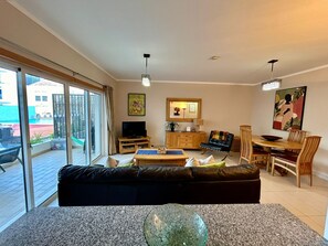 Relax in this stylish living room with a comfortable sofa, dining table for four, and large sliding glass door leading to an outdoor area.