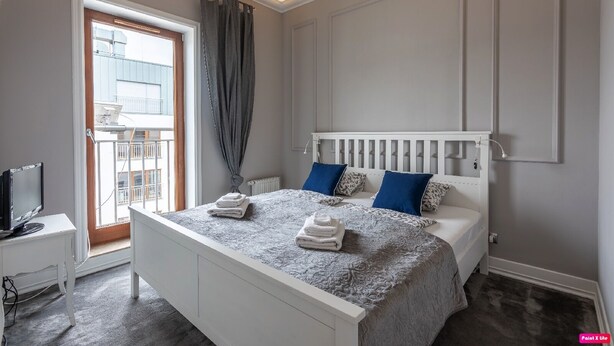 A bedroom with a large bed, a bedside table, a TV, and a view of the outside balcony.