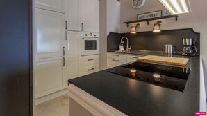 A modern kitchen with white cabinetry, a black countertop, a built-in oven, a coffee maker, and a clock on the wall.