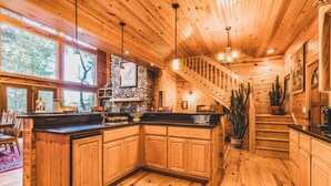 A wooden kitchen with a stone accent wall, a built-in island, and a staircase leading to an upper level. - MOUNTAIN HOME--GOLD STAR WINNER!--A peaceful place to breathe in, breathe out... (Hot Springs Village)
