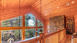 A wooden interior with large windows, a stone wall, and a bookshelf. - MOUNTAIN HOME--GOLD STAR WINNER!--A peaceful place to breathe in, breathe out... (Hot Springs Village)