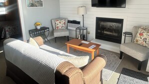 Una sala de estar con sofá, sillones, una mesa de centro, chimenea, televisor y un cuadro en la pared.