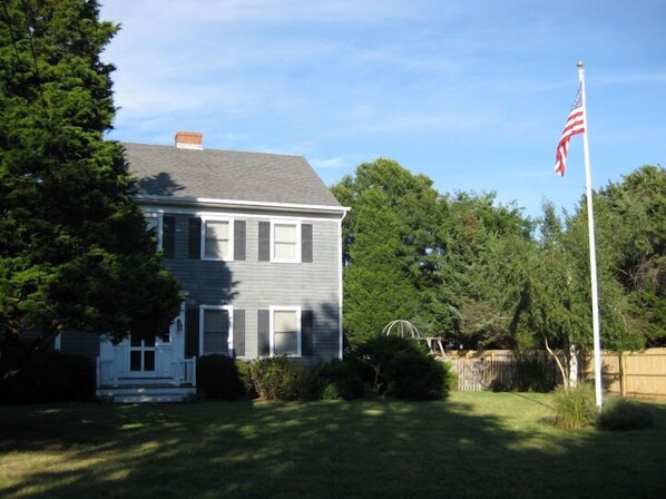 A two-story house with a front porch, a flagpole with an American flag, and a well-maintained lawn. - House by the Bay with Large In-ground Pool, Steps from Beach (East Marion)