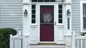 Une maison avec une porte d’entrée rouge, des moulures blanches et deux lampes de style lanterne de chaque côté.