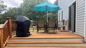 Une terrasse en bois avec des meubles d’extérieur, notamment une table et des chaises, ainsi qu’un barbecue couvert.