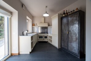 Eine kompakte Küche mit Herd, Spüle und Schränken, einem großen, dunklen Schrank und einem Fenster für natürliches Licht.