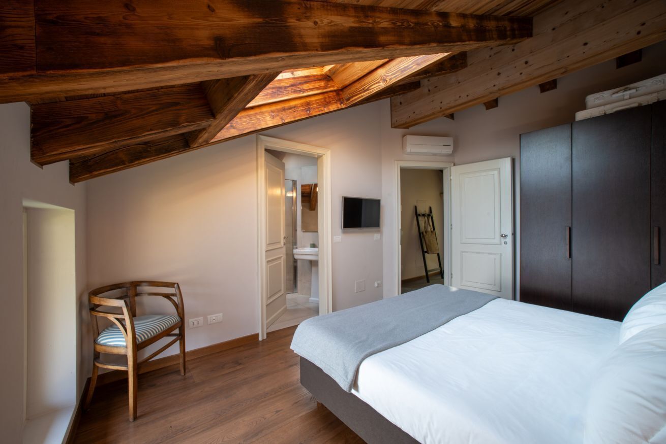 A bedroom with a wooden ceiling, a bed, a chair, and a wardrobe.