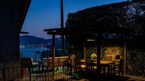 Eine Terrassengruppe im Freien mit Tisch und Stühlen, einer Pergola und Blick auf eine städtische Skyline im Abendlicht.