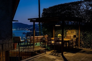 An outdoor patio with a table and chairs, a pergola, and a view of a cityscape at dusk.