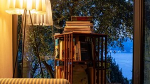 Ein Bücherregal mit Büchern, eine Lampe und Meerblick durch ein Fenster.