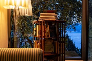 A bookshelf with books, a lamp, and a view of the sea through a window. - Toldino House 4 min. by car to lake (Cernobbio)