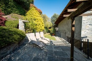 Un patio in pietra con poltrone relax, un muro in pietra e un pergolato in legno.