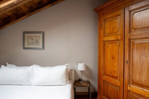 Een slaapkamer met een bed, een houten garderobe, een nachtkastje met een lamp en een ingelijst schilderij aan de muur.