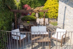 A covered outdoor seating area with a pergola, white cushioned chairs, and a table.