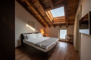 A bedroom with a wooden ceiling, a bed, a nightstand, and a window.