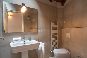 A bathroom with a sink, mirror, towel, toilet, and towel rack.