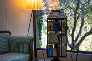 Een kamer met een raam, een lamp, een stoel en een boekenkast.