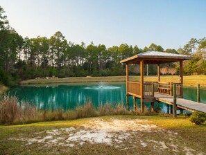 Un gazebo in legno con tetto metallico affacciato su un lago, circondato da alberi e prati.