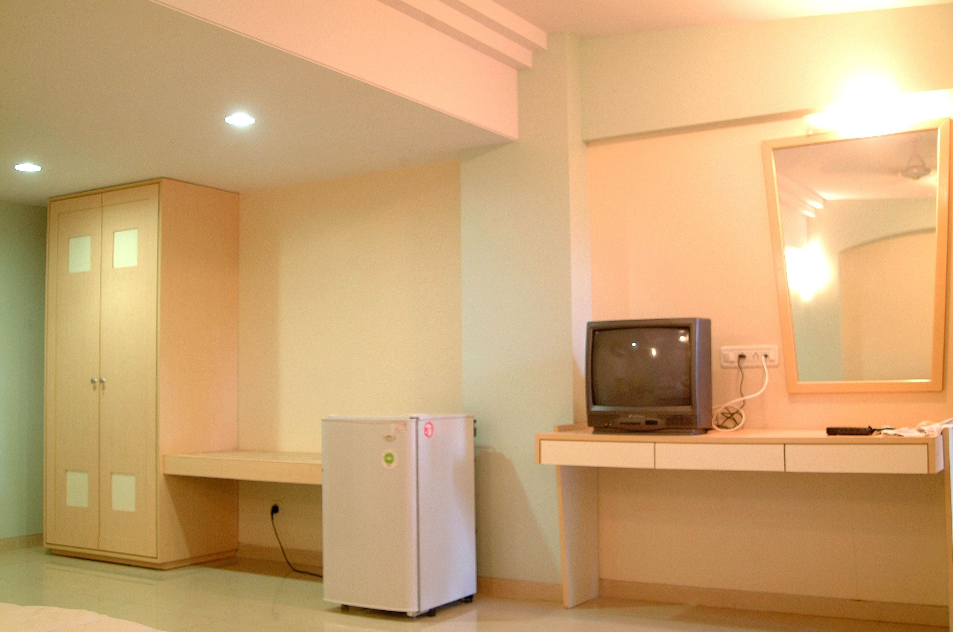 Una habitación con armario, refrigerador pequeño, televisor y espejo.