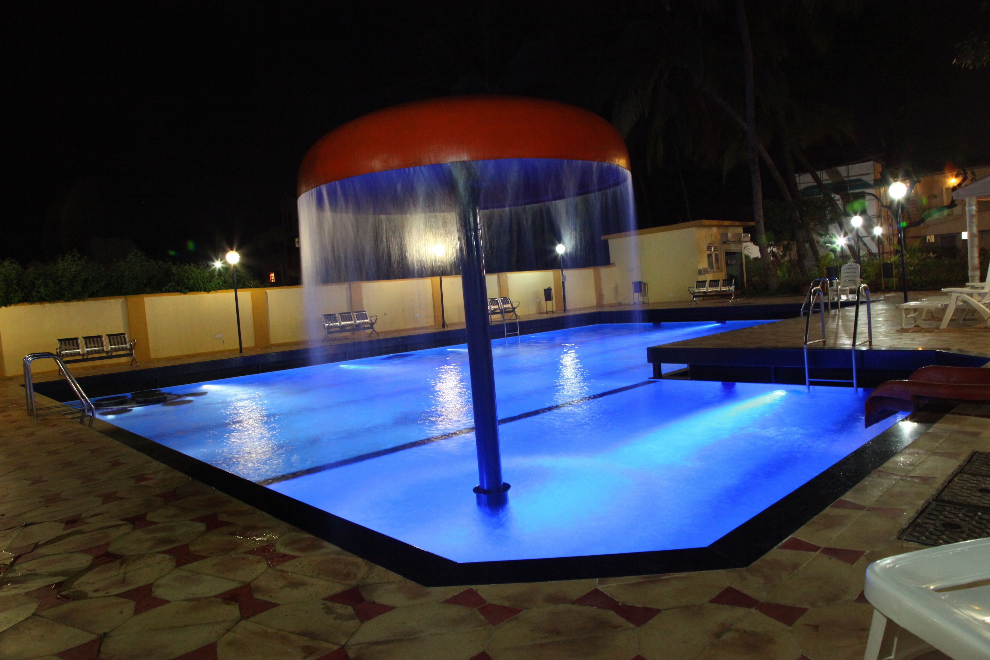 Una piscina con fuente, rodeada por una terraza con baldosas y bancos.