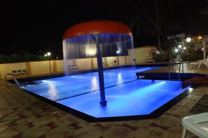 A swimming pool with a water feature, surrounded by a tiled deck and benches.