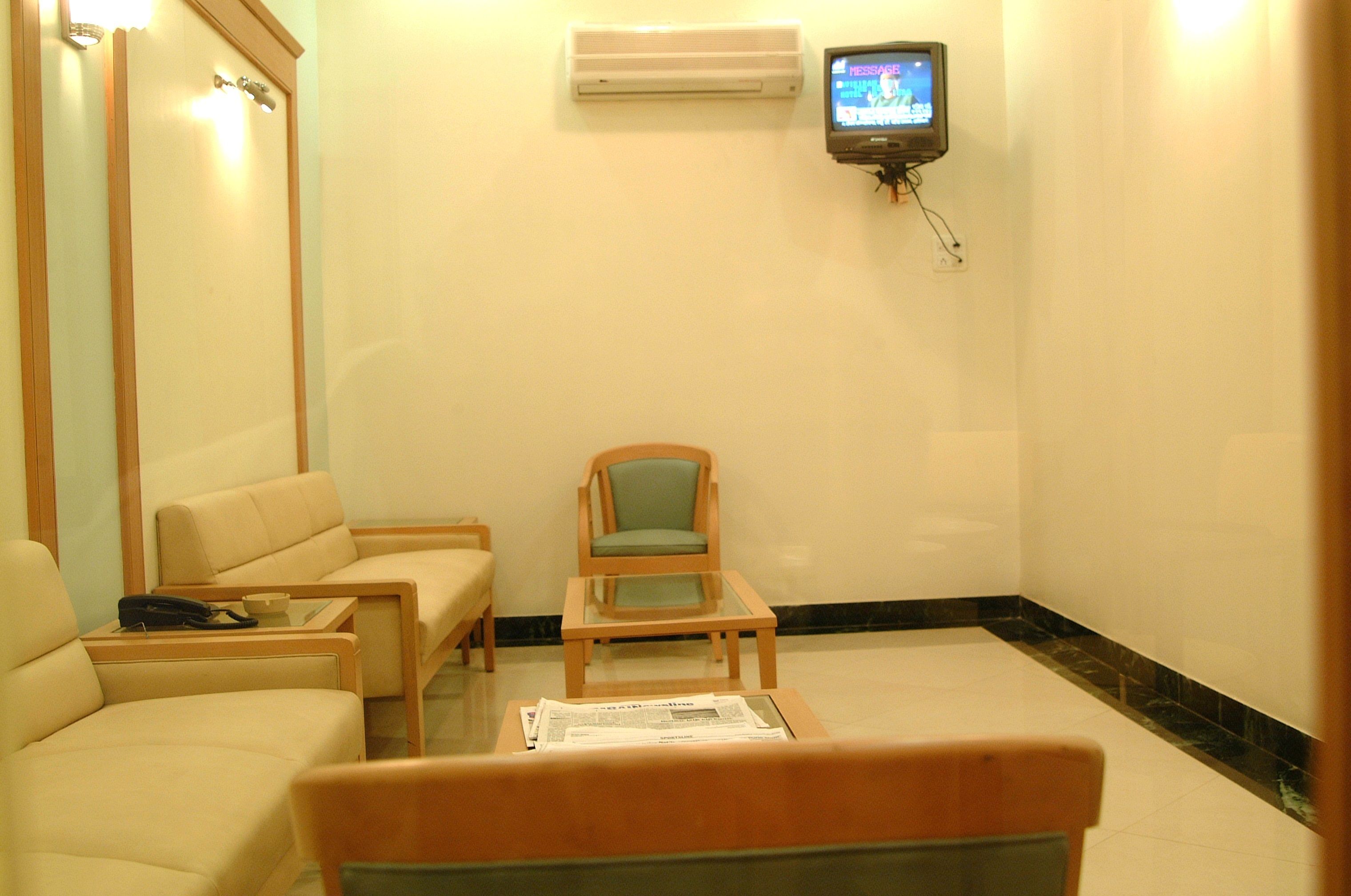 Habitación de hotel con sofá, una silla, una mesita y televisor montado en la pared.