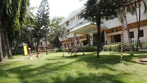 Un parque infantil con columpios y un tobogán, rodeado de árboles y un edificio con balcones.