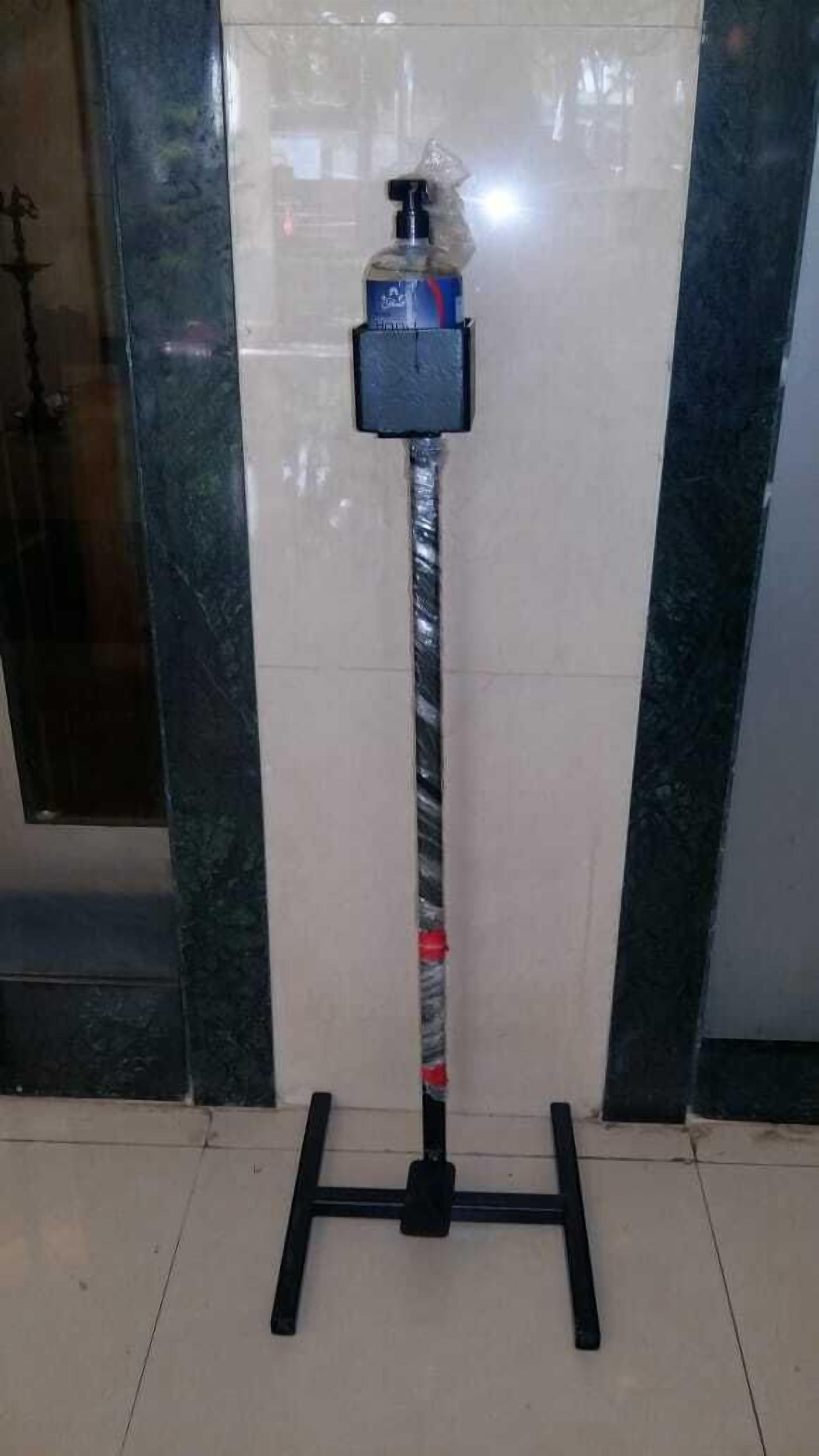 Un dispensador portátil de gel hidroalcohólico montado en un soporte con una barra de metal y una base.
