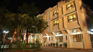 Un hotel de varios pisos con balcones y ventanas amplias, rodeado de palmeras y plantas en macetas.