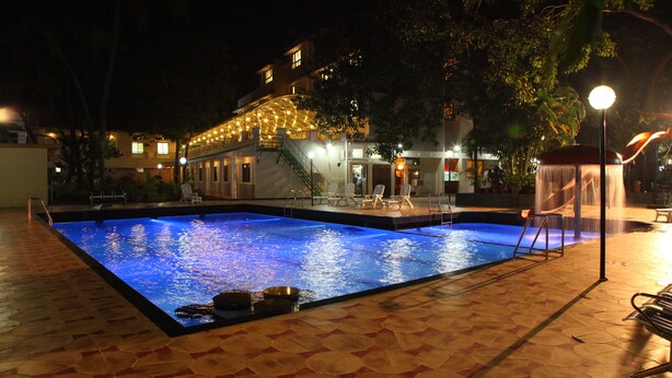 Una piscina con solárium empedrado, una escalera que conduce a un área techada y un edificio con luces colgantes al fondo.