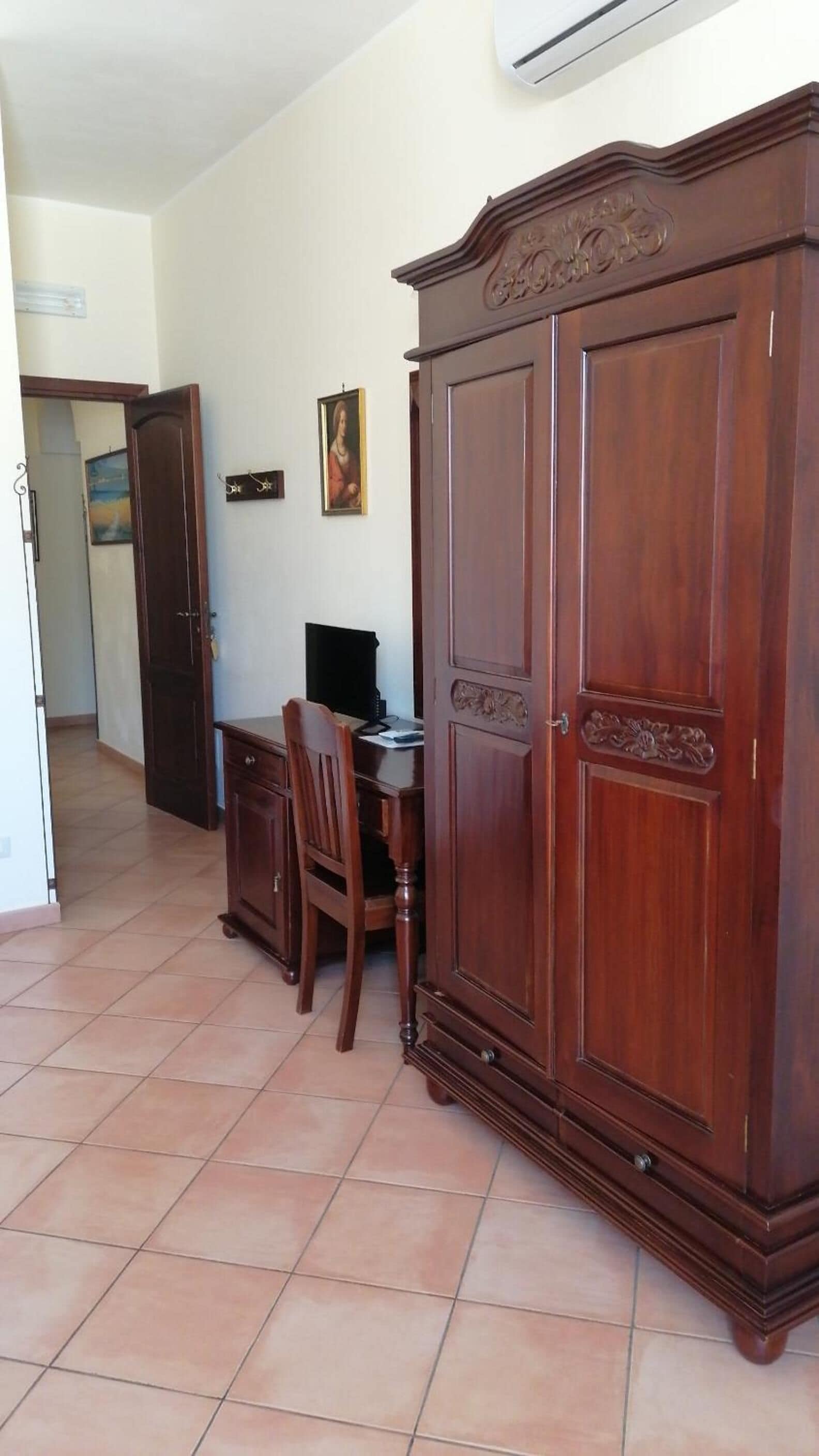 Una habitació amb un armari de fusta, un escriptori amb una cadira i un quadre a la paret.