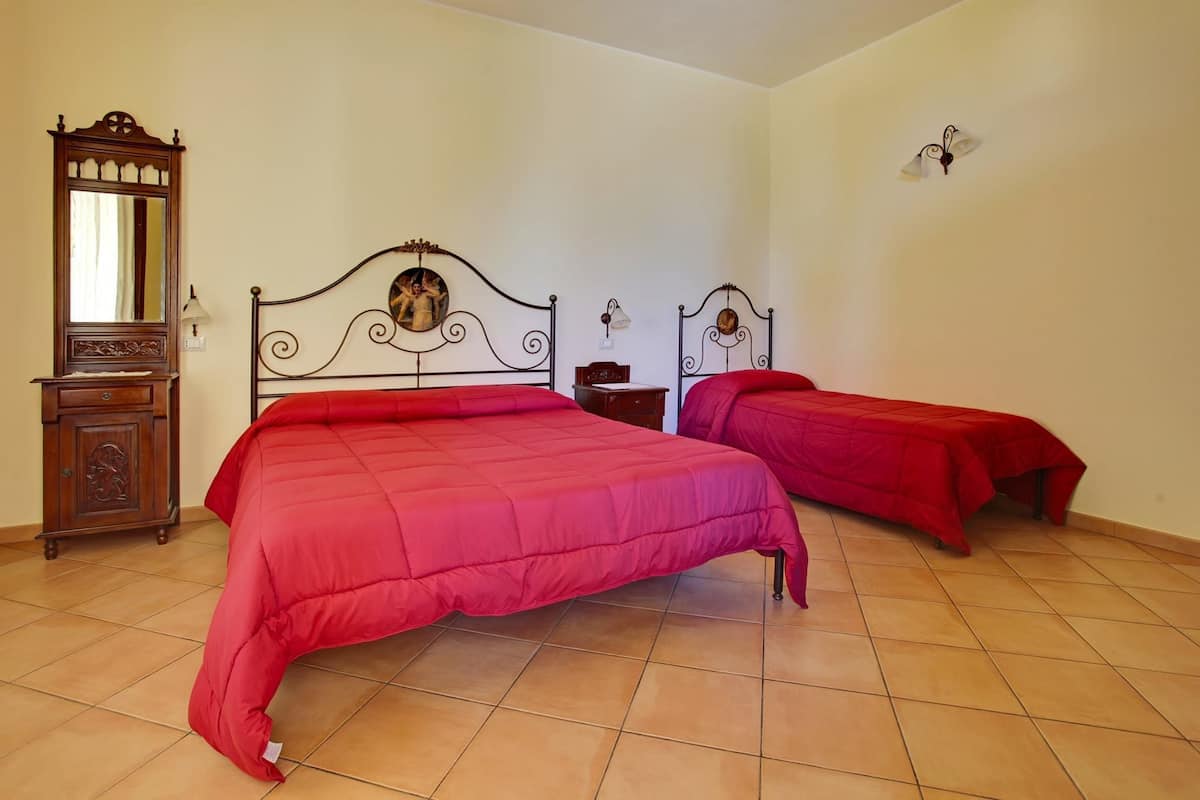 A bedroom with two beds, a wooden dresser, a mirror, and a wall-mounted lamp.