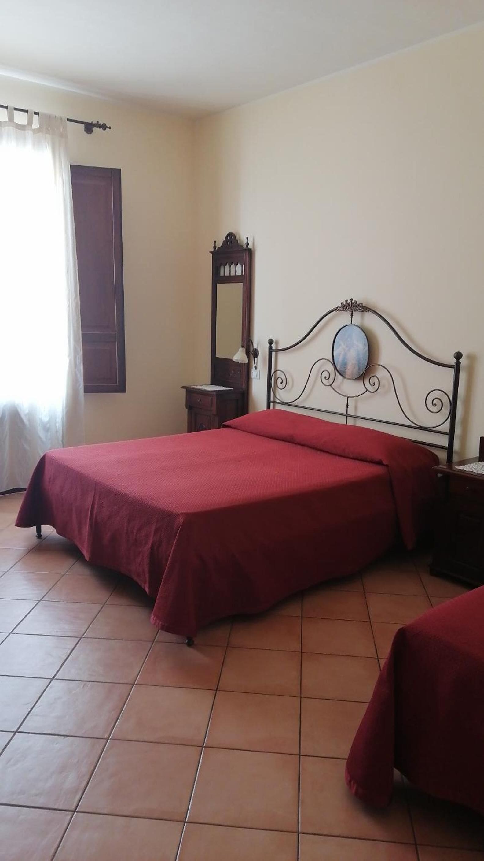Una camera da letto con un letto, un comodino, uno specchio e una finestra con tende.