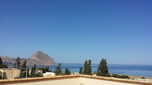 A coastal view with a mountain, clear sky, and a building with a balcony. - Kalura (San Vito Lo Capo)