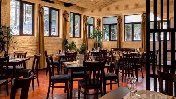 Ein Restaurant mit Backsteinwänden, großen Fenstern und Holztischen und -stühlen.