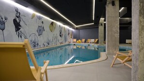 Ein Innenpool mit Wandmalerei, Liegestühlen und einem modernen Deckenbau.