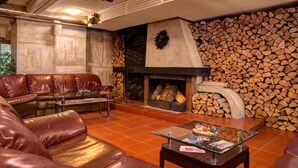 Ein gemütliches Wohnzimmer mit Ledersofas, einem Glastisch und einem Kamin mit Holzvorrat.
